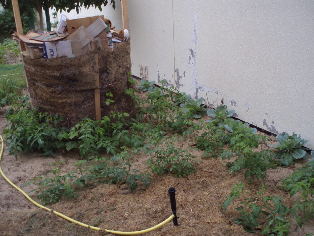 Photo shows compost pile overed with cardboard boxes to keep critters out and shield the compost from the sun.  If you cover it, be sure to remember to remove the cardboard and water it anyway.